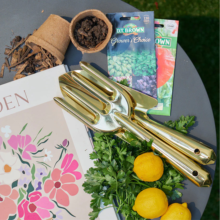 The Annabel Trends Garden Tool Set in Gold on an outdoor table with lemons, parsley and garden supplies