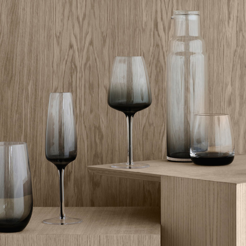 The Broste Copenhagen Champagne Glass in Smoke on a shelf with other Broste glassware