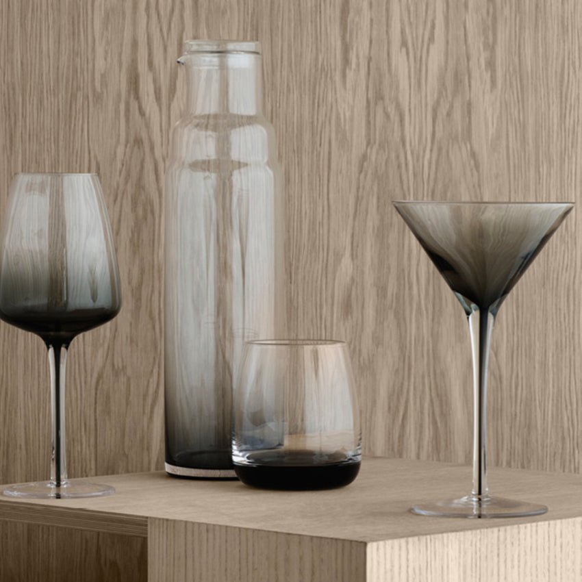 The Broste Copenhagen Martini Glass in Smoke on a table with other glassware
