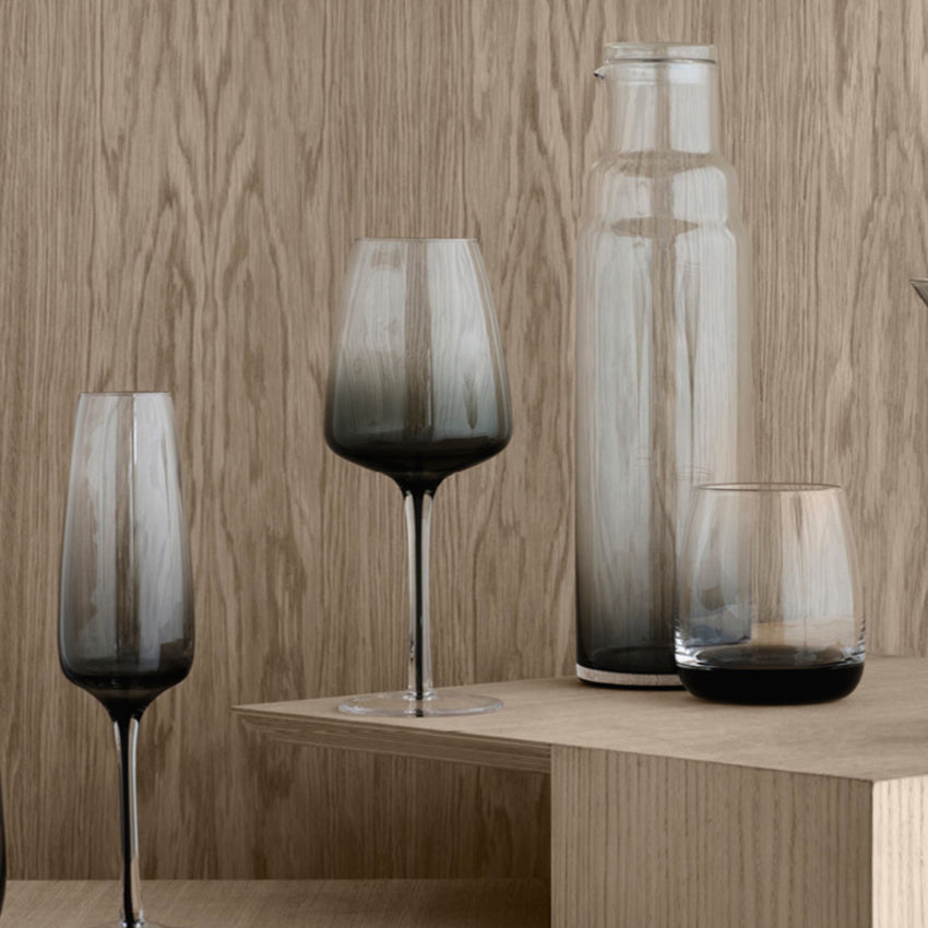 The Broste Copenhagen White Wine Glass in Smoke on a shelf with other glassware