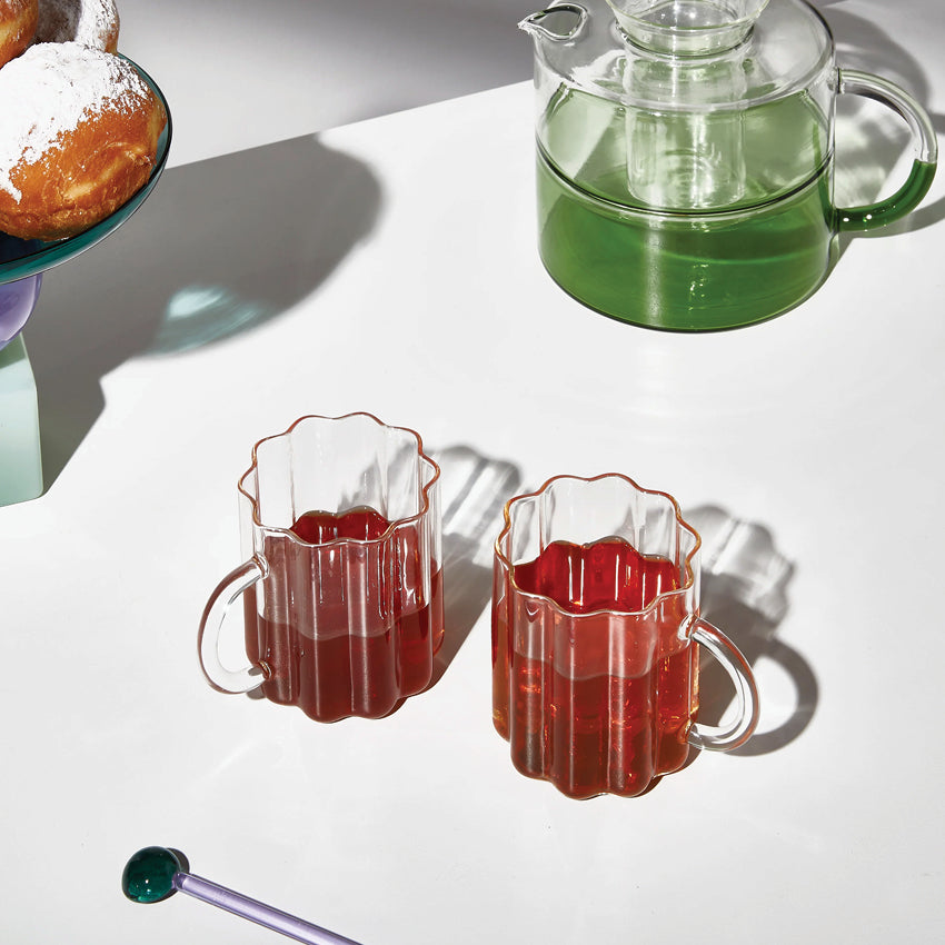 The Fazeek Wave Mugs in Clear on a table with tea in them next to the Fazeek teapot and cakestand