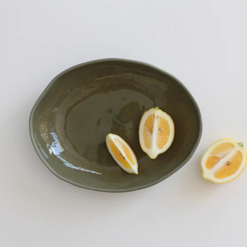 The JS Ceramics Large Oval Bowl in Sage Green with lemon slices in it on a blank background