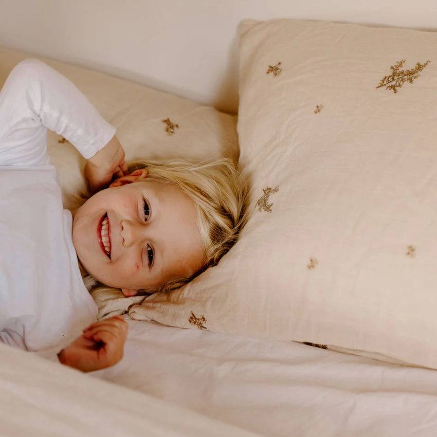 Leni The Label Muslin Pillowcase in Kanuka on a bed with a girl lying on them