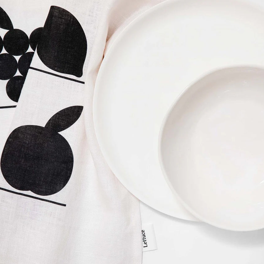 The Lettuce Linen Tea Towel in Fruit Shelf design under white plates