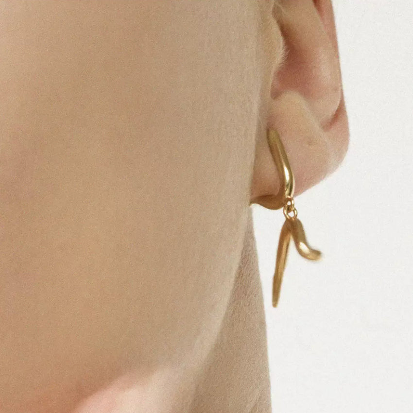 The Meadowlark Sculpture Drop Earrings in Gold Plated on a model.