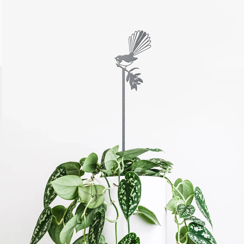 The Metalbird Piwakawaka Plant Stake in a pot with a plant on a blank background