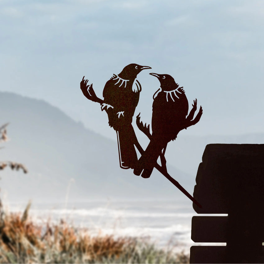 The Metalbird steel Tui Pair in a wooden seat with a beach in the background