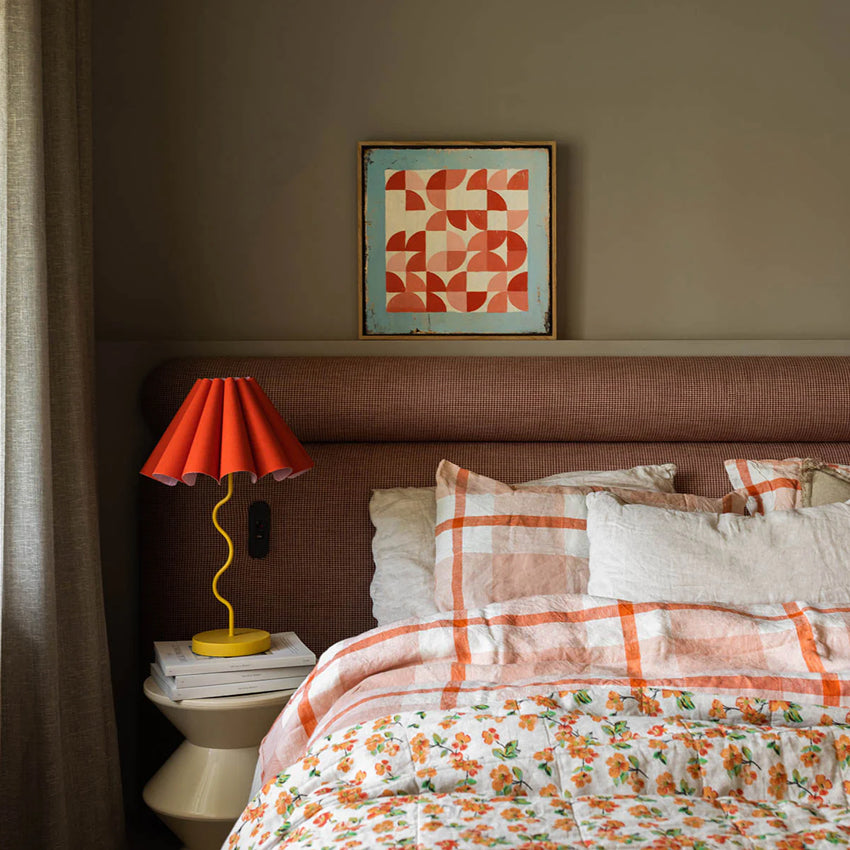 The Paola and Joy Cora Table Lamp in Rouge Mustard next to a bed on a bedside table