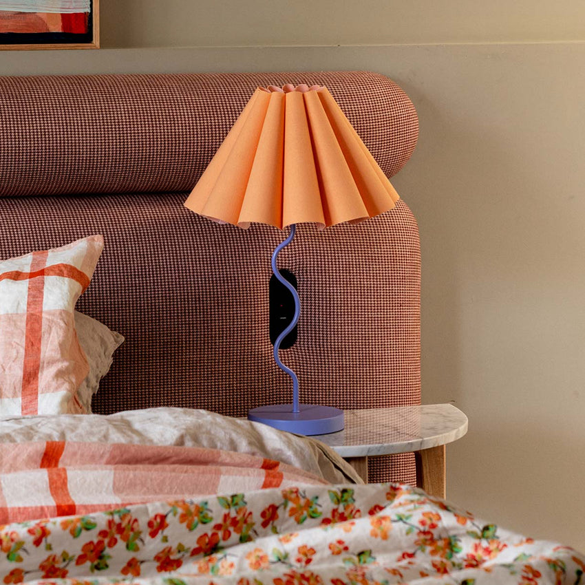 The Paola and Joy Cora Table Lamp in Tropical Peach and Purple on a bed side table next to a bed