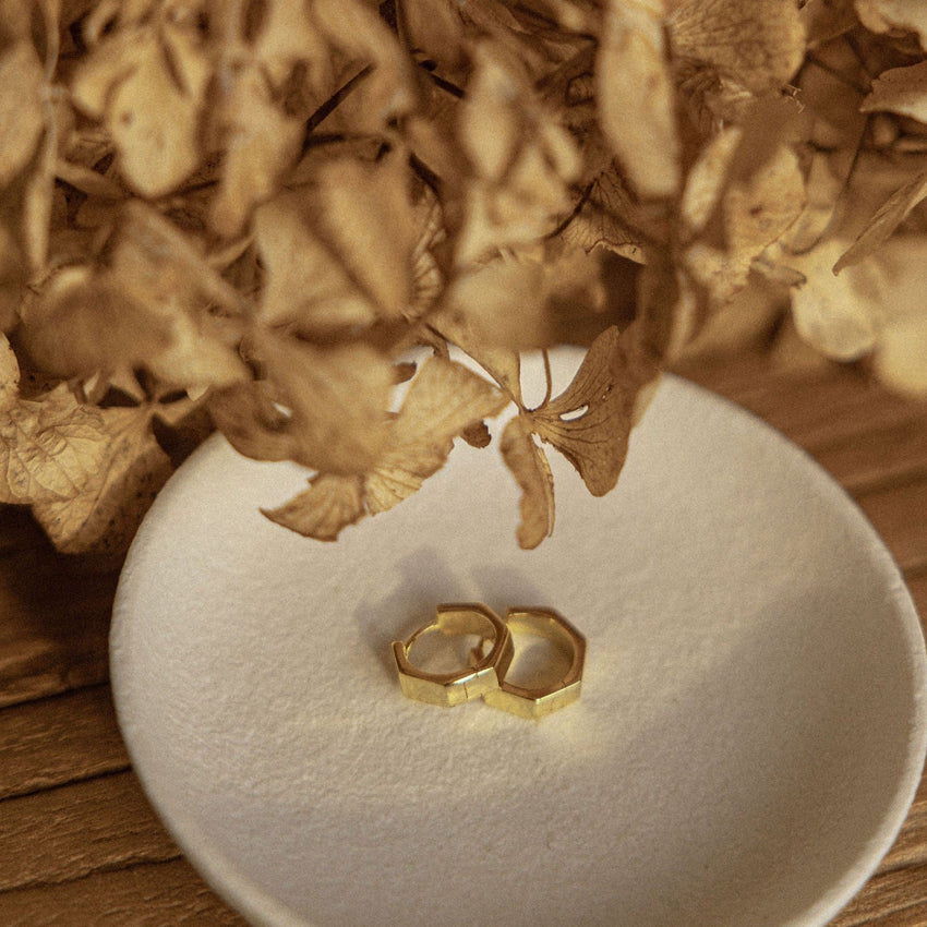 The Silver Linings Collective Whistledown Solid Hoops in Gold on a textured bowl with some flowers