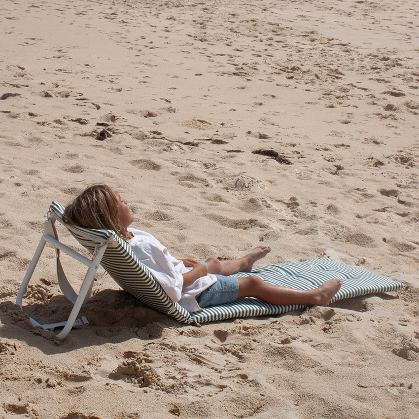 The Sunnylife Reclining Beach Chair in Olive on the beach with a kid lying on it