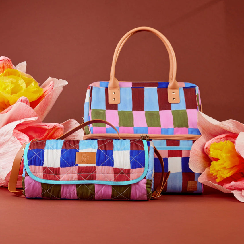 The Somewhere Co XL Picnic Rug in Hopscotch next to a matching cooler bag next to flowers