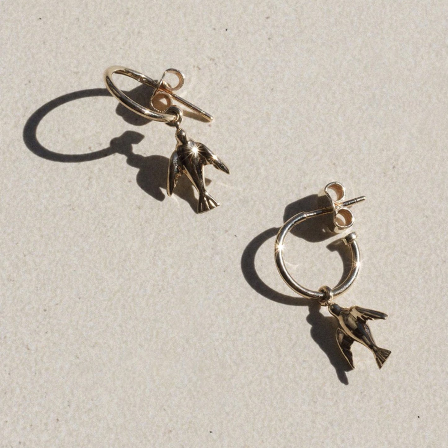 The Meadowlark Dove Signature Hoops in Gold Plated on a textured background.
