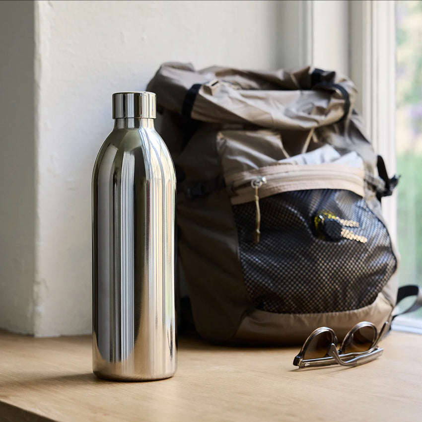 The Aarke C3 Insulated Stainless Steel Bottle 1000ml on a window ledge next to a backpack