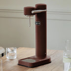 The Aarke Carbonator 3 in Burgundy on a table next to a glass