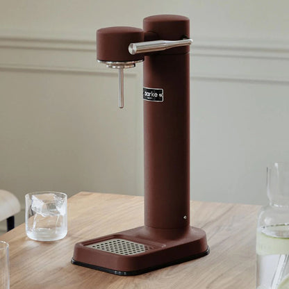 The Aarke Carbonator 3 in Burgundy on a table next to a glass