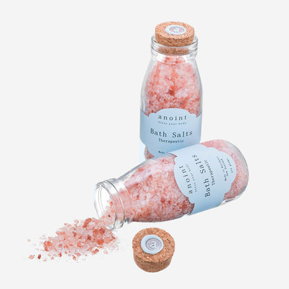 Two of the Anoint Bath Salts bottles with one spilling out on a blank background