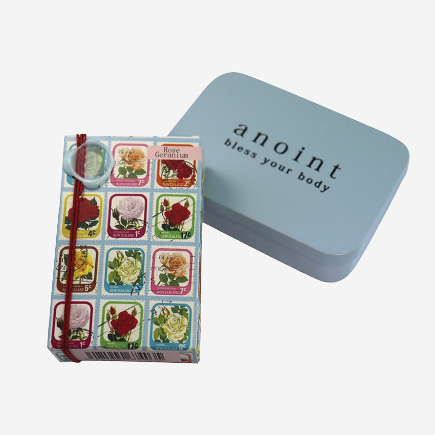 The Anoint Rose Geranium Lotion Bar next to its tin on a blank background