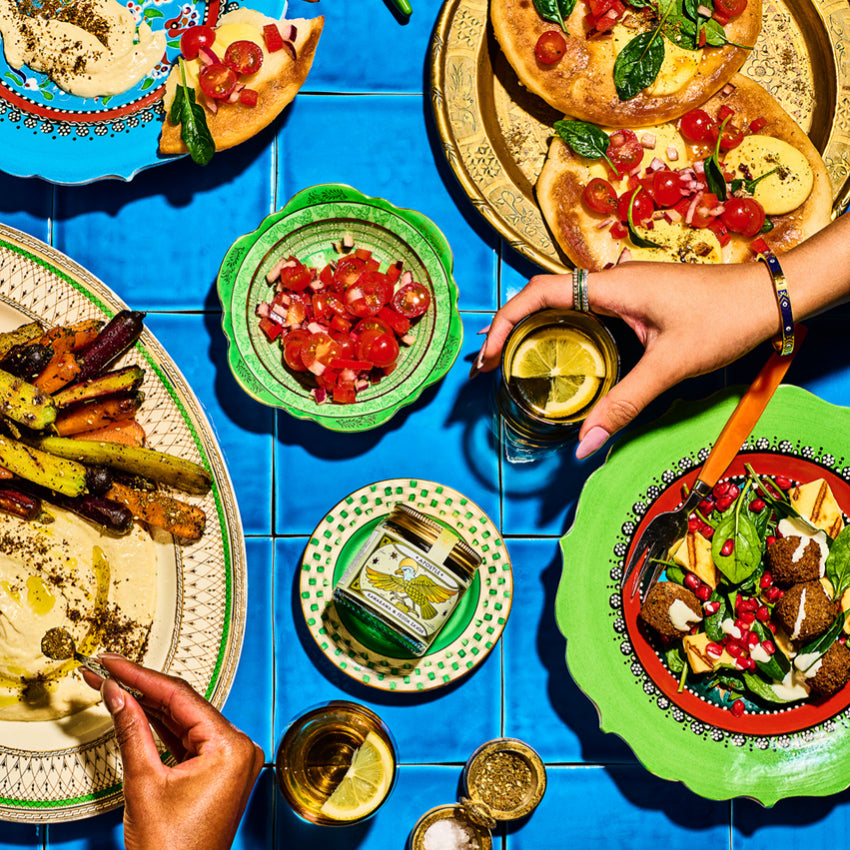 The Apostle Kawakawa and Feijoa Za'atar Seasoning jar on a blue tiled table surronded by food dishes