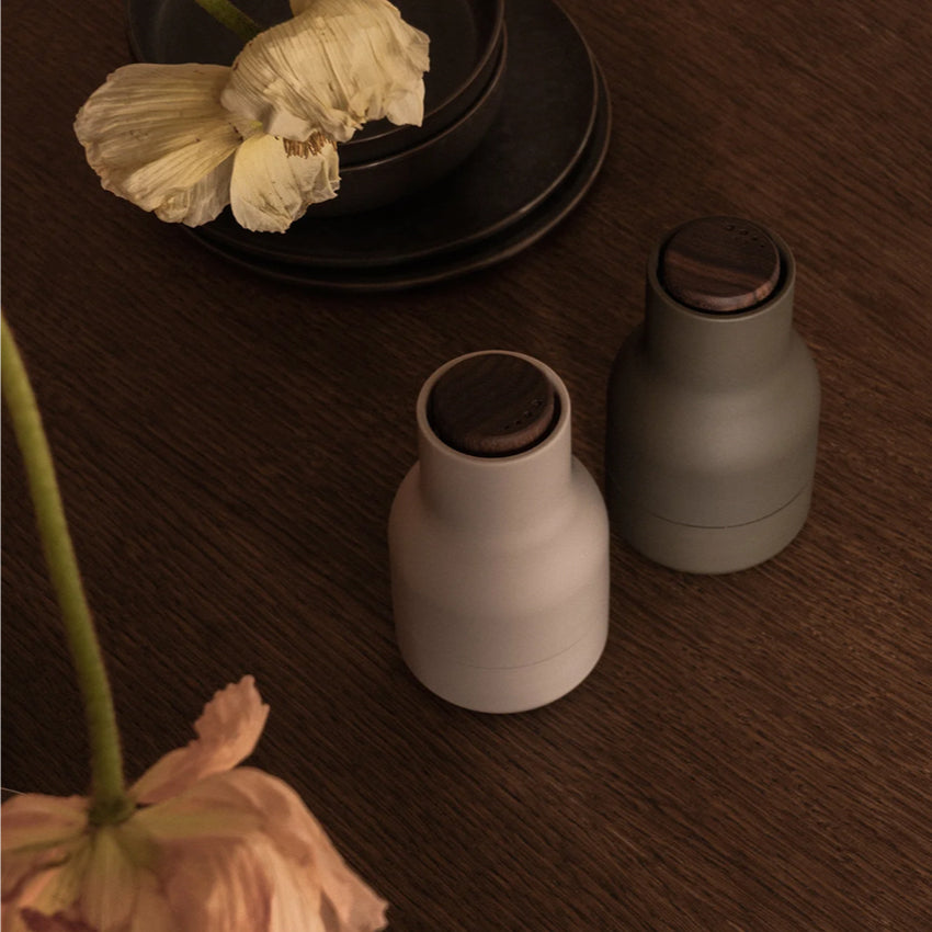 The Small Audo Salt and Pepper Grinder in Hunting Green and Walnut 
 on a table with flowers and plates