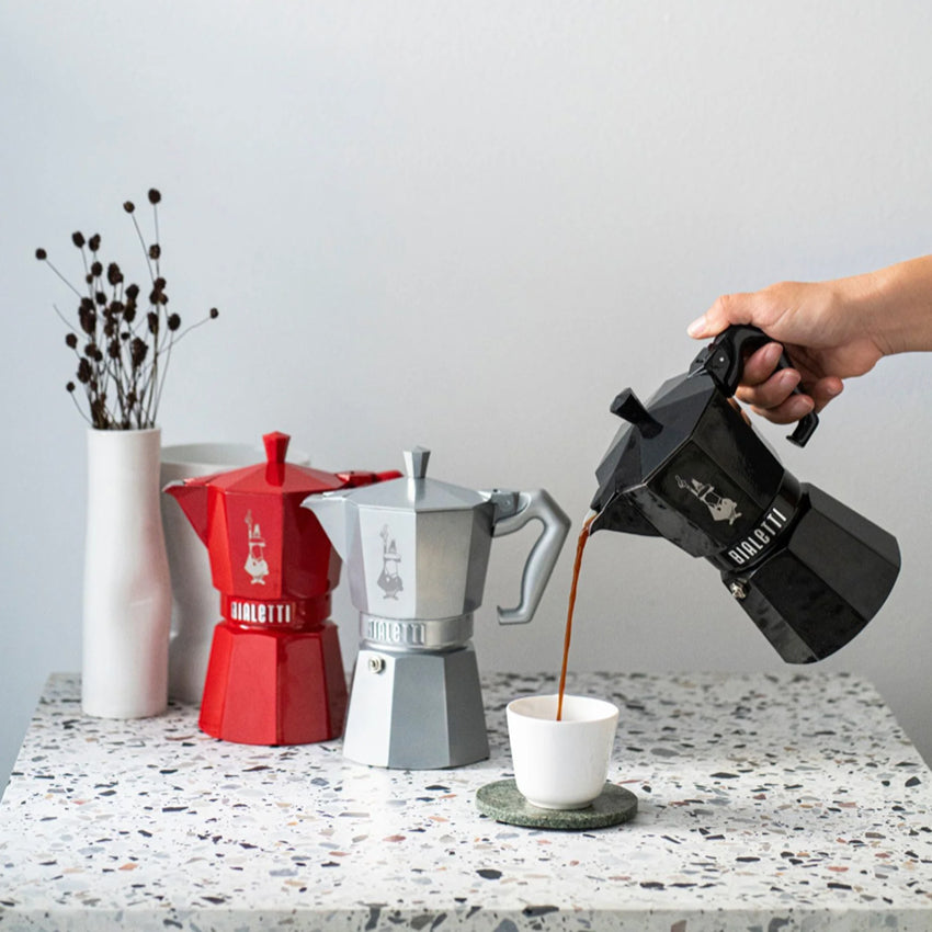 The Bialetti Moka Exclusive Coffee Pot 6 cup size in Black with coffee being poured into a cup