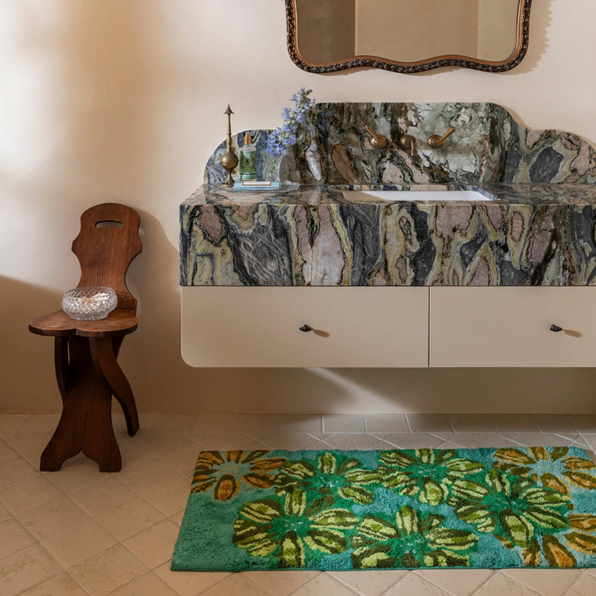 The Bonnie and Neil Candy Teal Bath Mat on a bathroom floor under a marble vanity