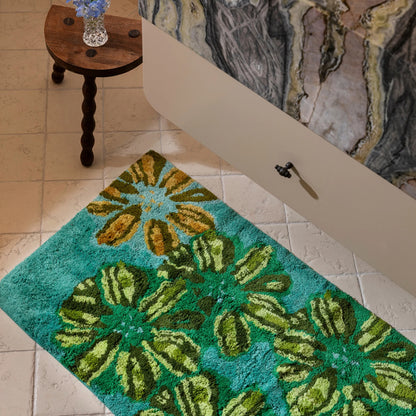 The Bonnie and Neil Candy Teal Bath Mat on a bathroom floor under a marble vanity