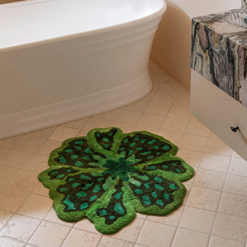 The Bonnie and Neil Flower Bath Mat in Green on a tiled bathroom floor next to a bath and marble vanity