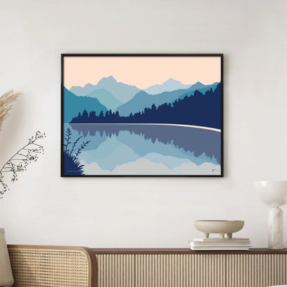 A modern mountain art print of Lake Matheson in tones of blue and pink by Bridget Hall in a black frame hanging on a wall
