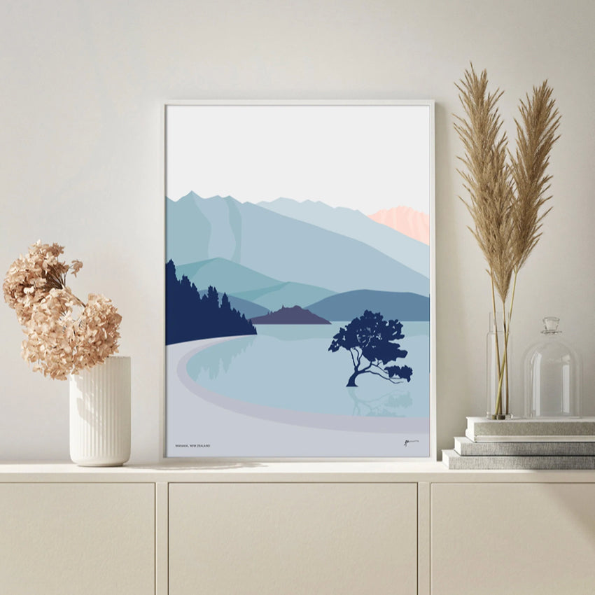 The Bridget Hall Designs Wanaka Tree Vertical Art Print in a frame on a shelf next to plants