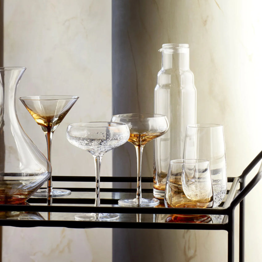 The Broste Copenhagen Cocktail Glass in Amber on a bar cart with other Broste glassware