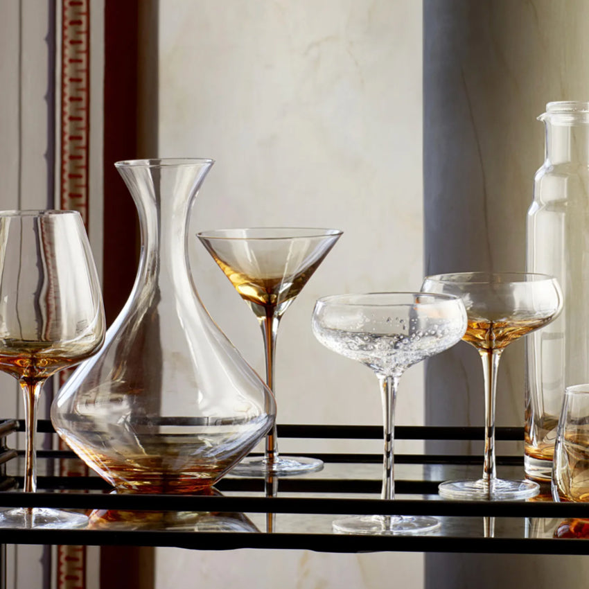 The Broste Copenhagen Martini Glass in Amber on a bar cart with other Broste glassware