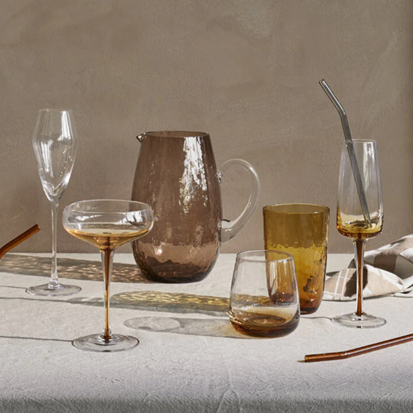 The Broste Copenhagen Short Tumbler Glass in Amber on a table with other Broste Glassware surrounding 