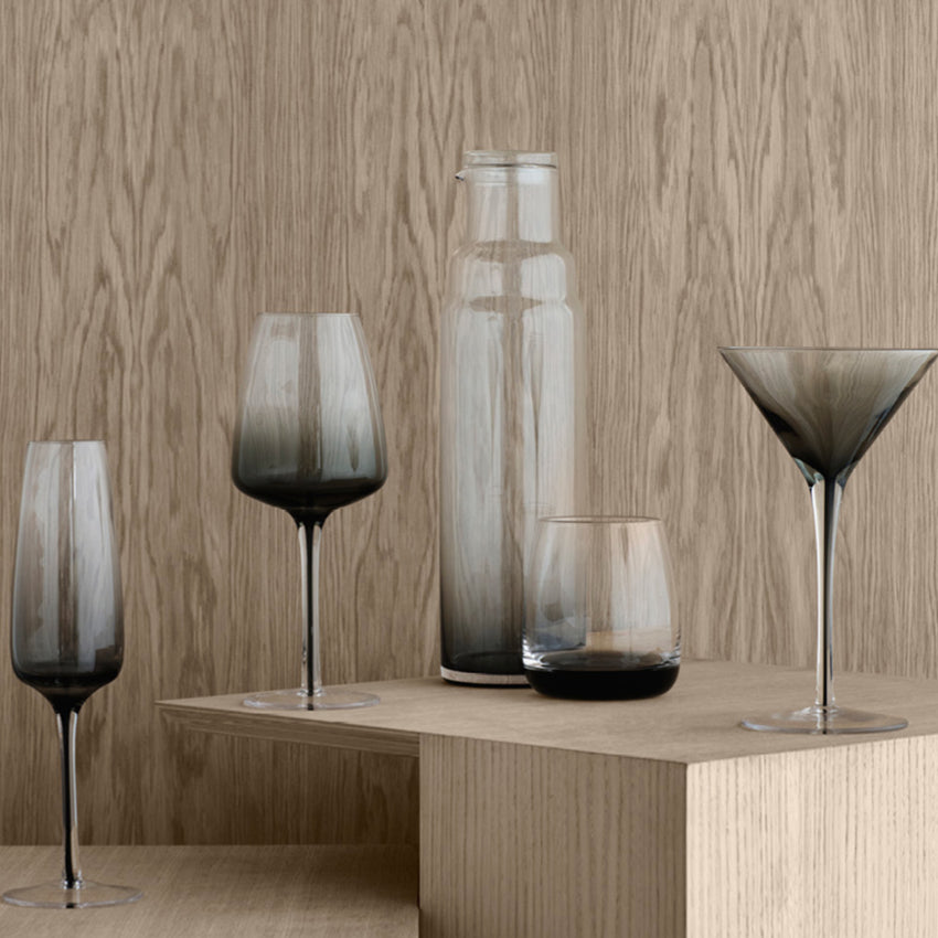 The Broste Copenhagen Short Tumbler Glass in Smoke on a shelf with other glassware