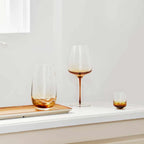 The Broste Copenhagen Tall Tumbler Glass in Amber on a shelf with other Broste glassware