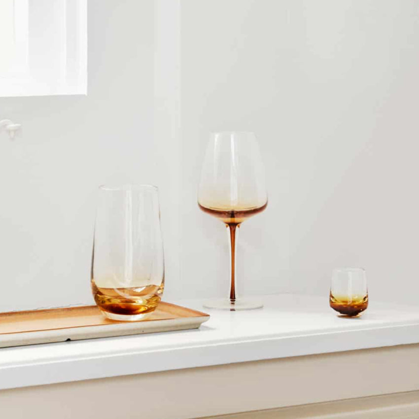 The Broste Copenhagen Tall Tumbler Glass in Amber on a shelf with other Broste glassware