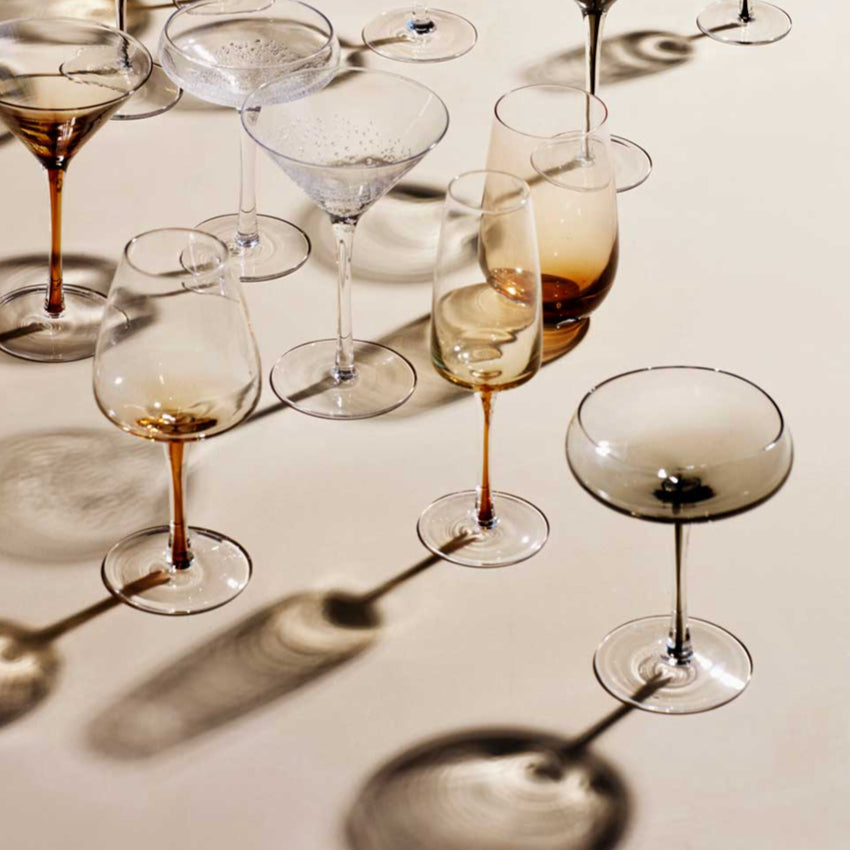 The Broste Copenhagen White Wine Glass in Amber surronded by other Broste glassware
