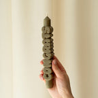 A hand holding the Candle Hand Congrats 3D Taper Candle in olive
