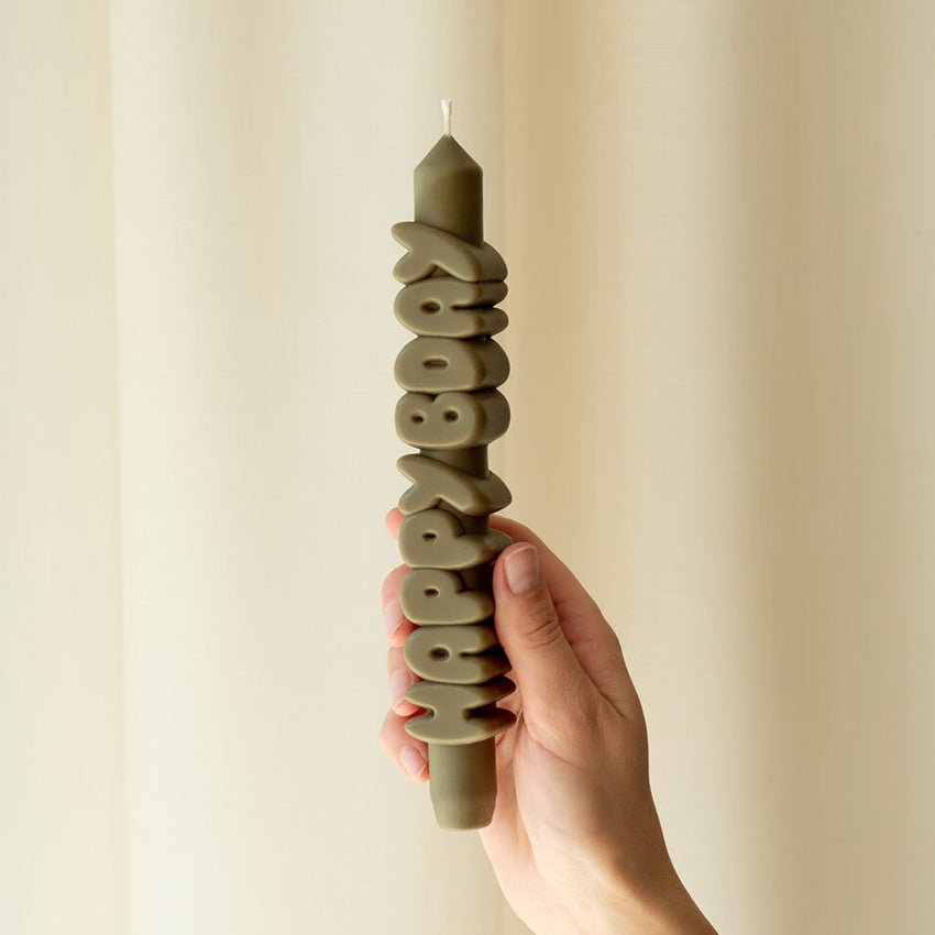 A hand holding the CandleHand Happy Bday Taper Candle in olive
