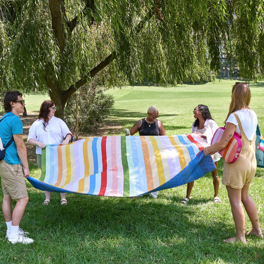 A group of people holding up the  Dock & Bay Picnic Blanket in Candy Stripe on a grey background