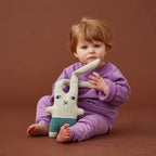 The Donna Wilson Wee One Bonnie Bunny with a baby in a purple outfit on a brown background