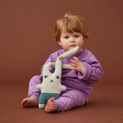 The Donna Wilson Wee One Bonnie Bunny with a baby in a purple outfit on a brown background