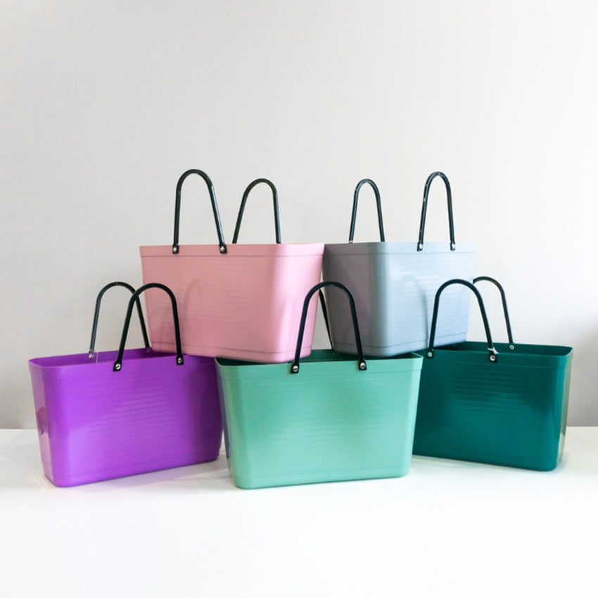 A collection of Hinza bags in various colours including purple, pink, green, and teal, displayed against a neutral background.