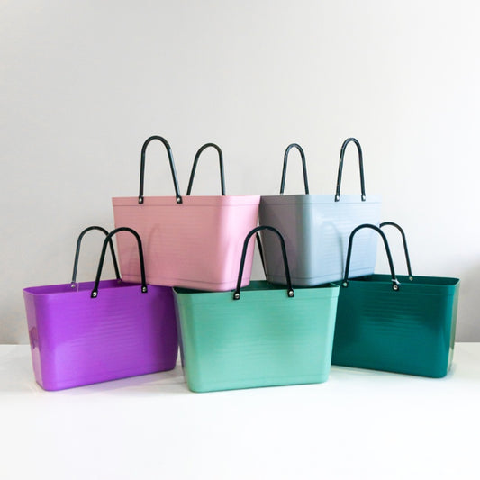 A collection of Hinza bags in various colours including purple, pink, green, and teal, displayed against a neutral background.