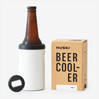 The Huski Beer Cooler in White with a beer bottle in it next to its box on a blank background