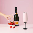 The Huski Champagne Flute in pink next to a bottle of champagne and a bowl of strawberries