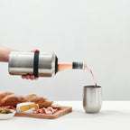 The Huski Wine Cooler in Brushed Stainless with a wine bottle in it being poured into a huski Wine Tumbler and next to a cheese board