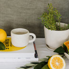 The JS Ceramics Ceramic Mug in Oatmeal in a kitchen setup on top of cookbooks