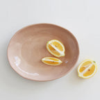 The JS Ceramics Large Oval Bowl in Pink Sand with lemon slices in it on a blank background