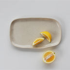 The JS Ceramics Rectangle Platter in Oatmeal with lemon slices on it on a blank background
